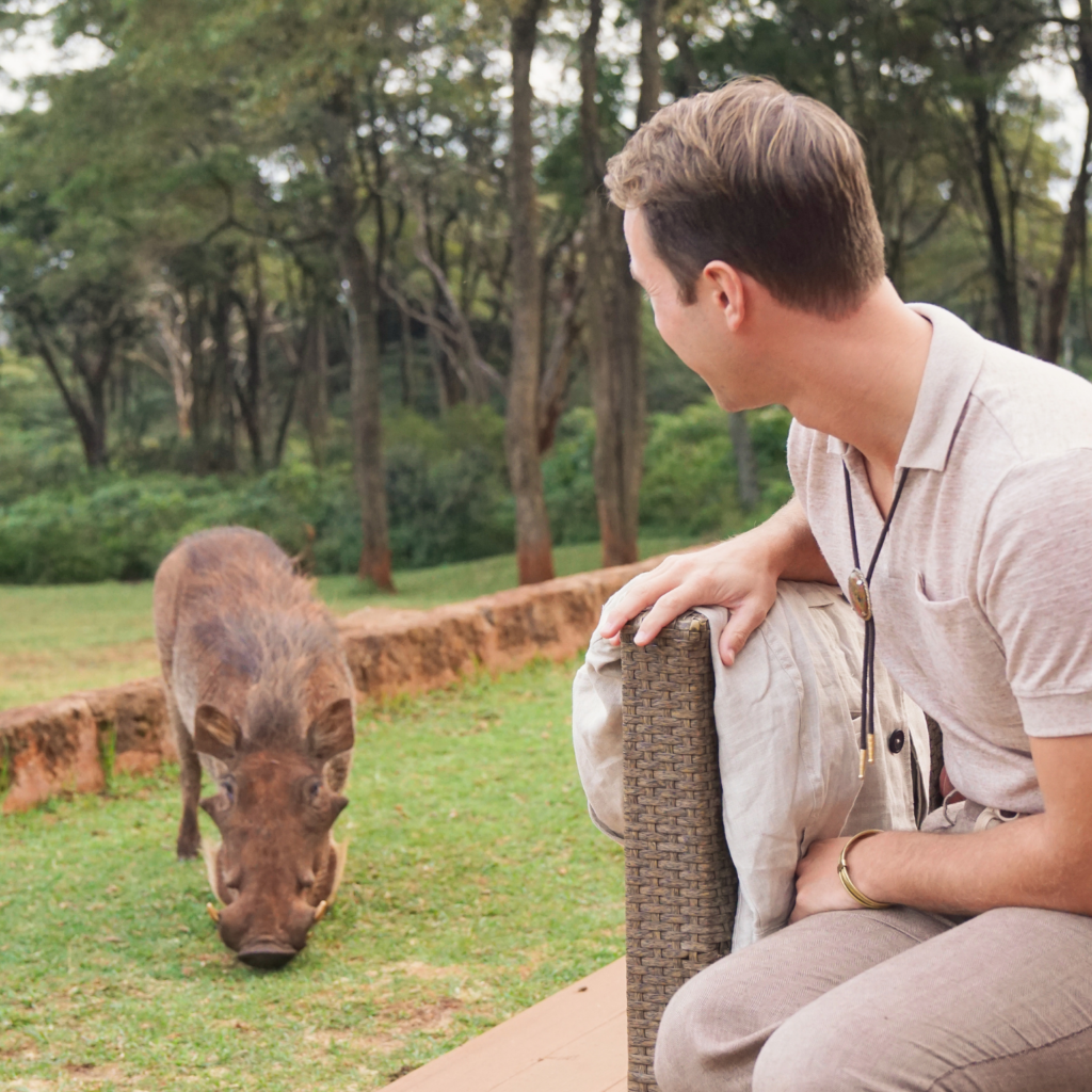 young man watching a warthog at Giraffe Manor