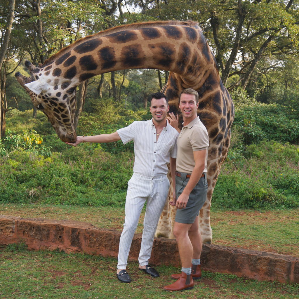 a gay couple feeding a giraffe at Giraffe manor in Nairobi, Kenya